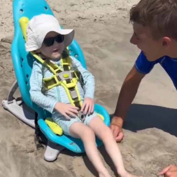 Un niño se sienta en la playa en su asiento de baño multiusos Splashy.