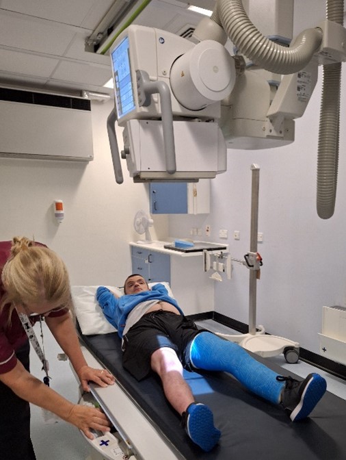 Un jeune homme passe une radiographie de sa jambe blessée et plâtrée en bleu.