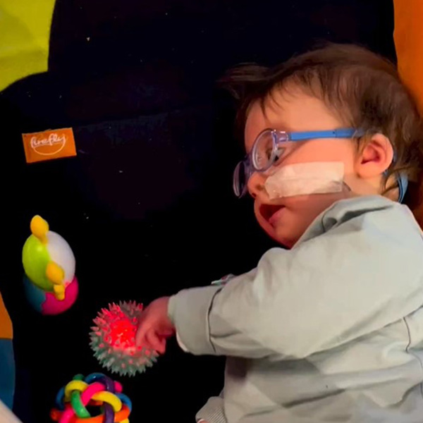 Niño tumbado de lado utilizando la alfombrilla de juego Playpak de intervención temprana para apoyarse mientras juega con juguetes sensoriales.