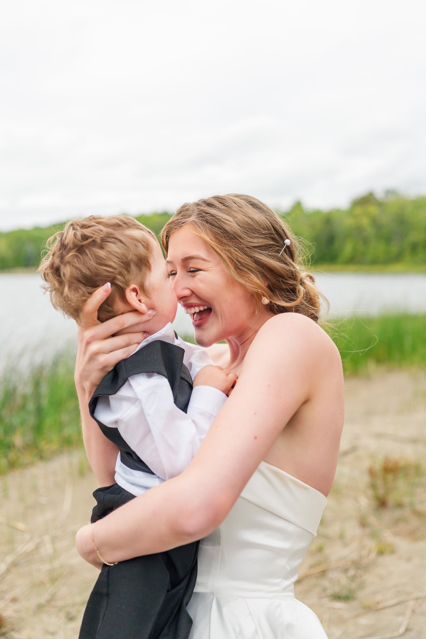 A mother in a wedding dress holds her son while they smile close;y at each other.