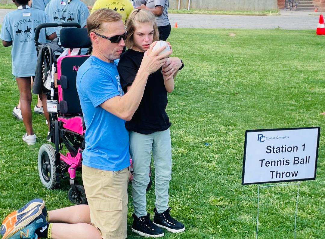 A father helps his daughter throw a tennis ball