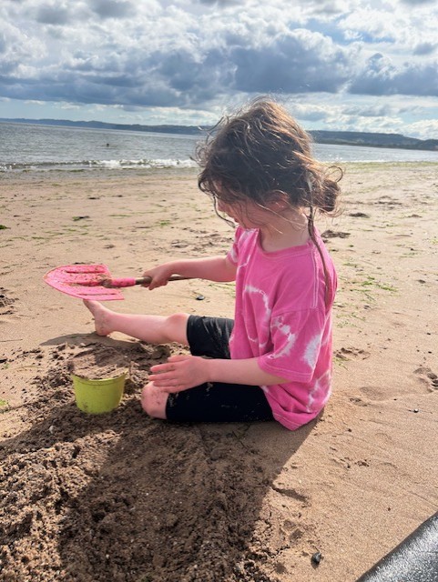 A little girl plays with a bucket and spade on the beach