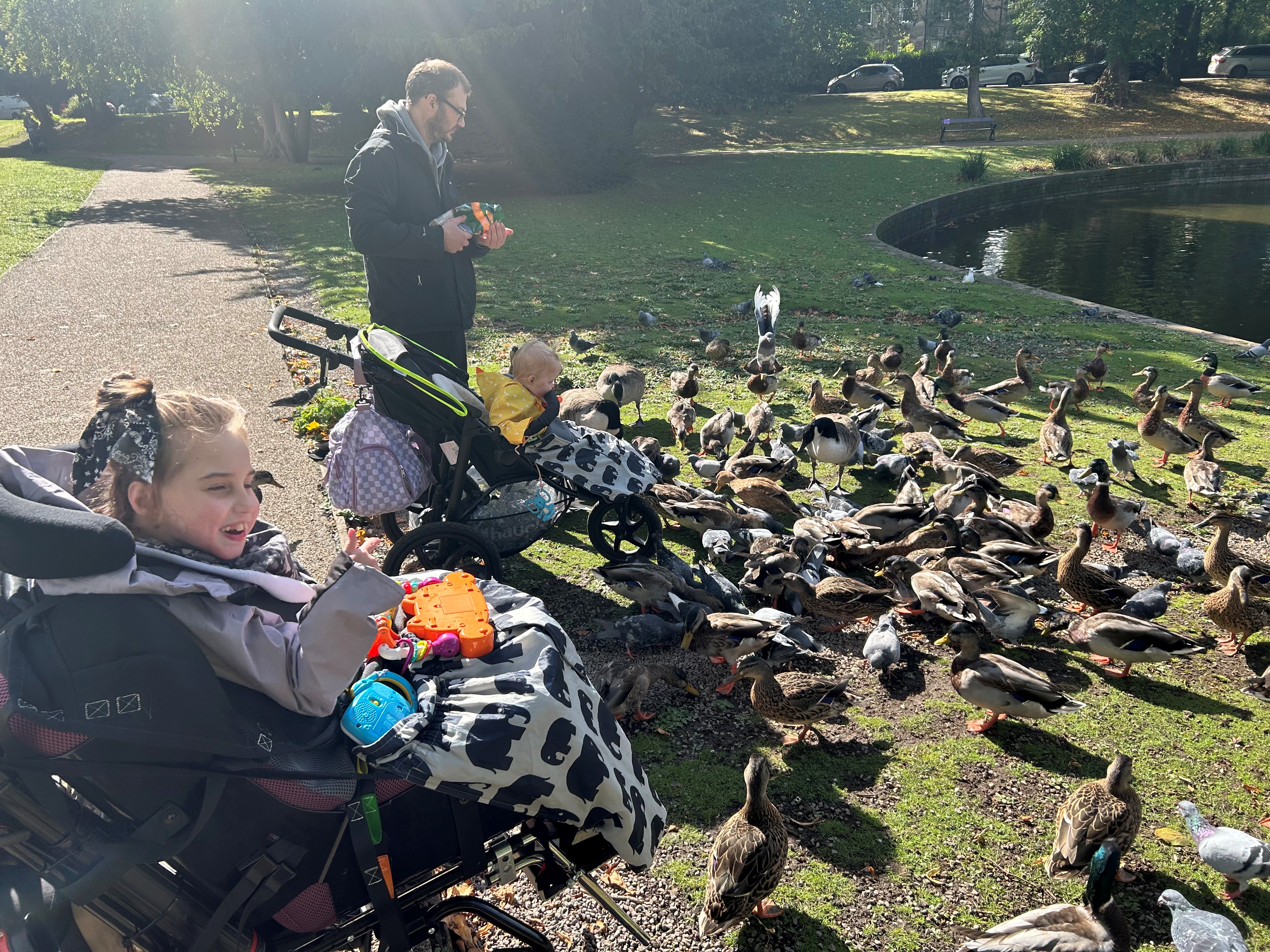 A father and 2 daughterswatch the ducks at the park