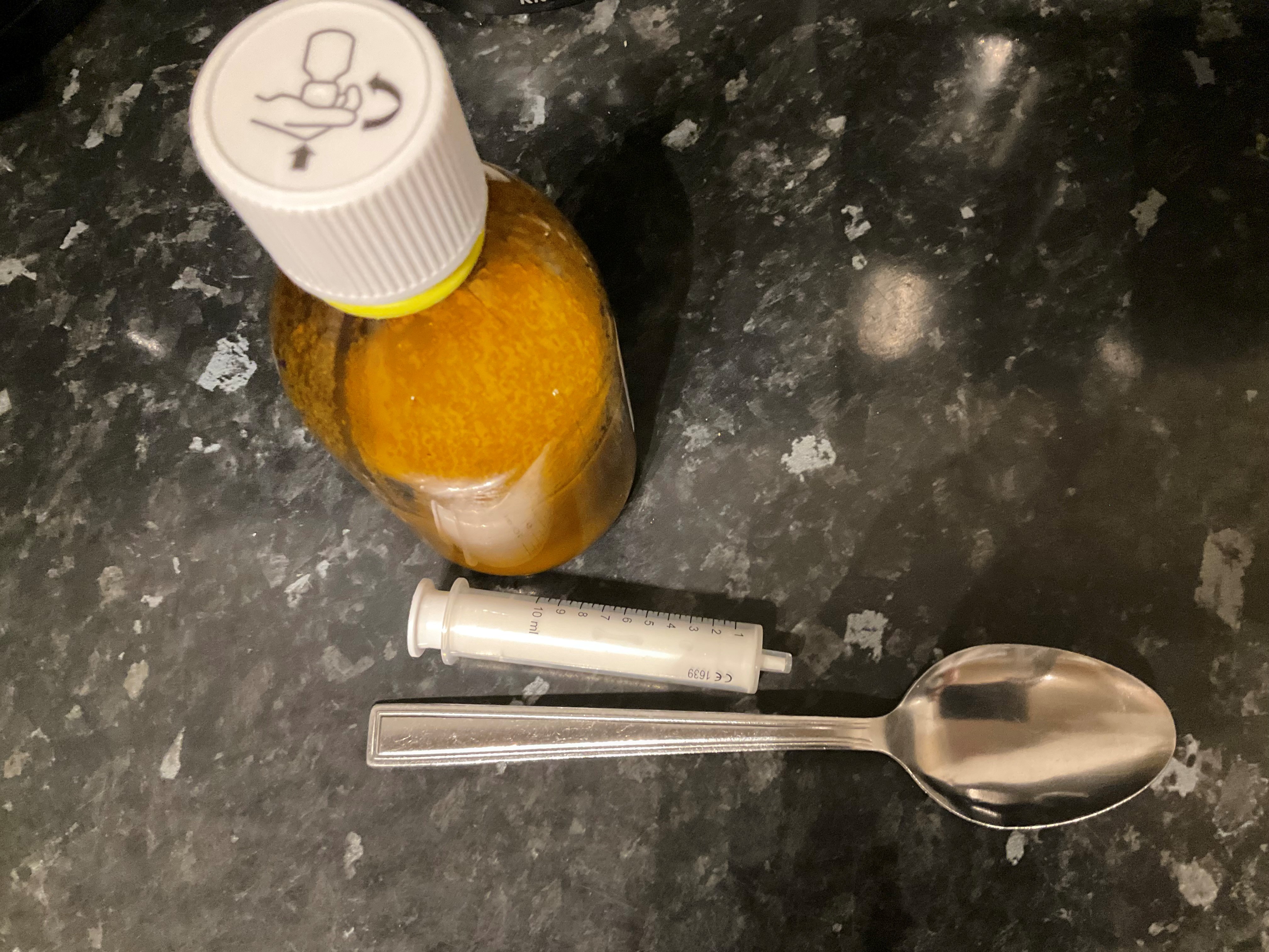 A medication bottle and 2 spoons sit on a countertop