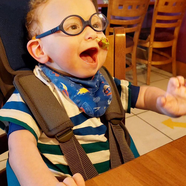 Young boy wearing glasses looking happy whilst sitting at a table in a restaurant with the help of a GoTo Seat