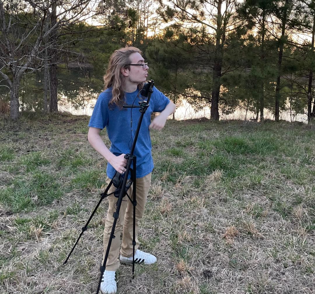 A young man with a camera tripod films outdoors