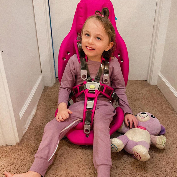 A little girl smiles while sitting on the floor supported in her Splashy multipurpose bath seat.