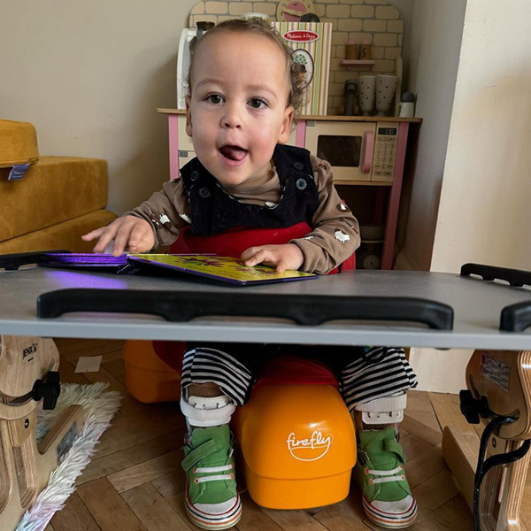 Un niño se sienta en la mesa de su guardería en su Scooot sit and ride.