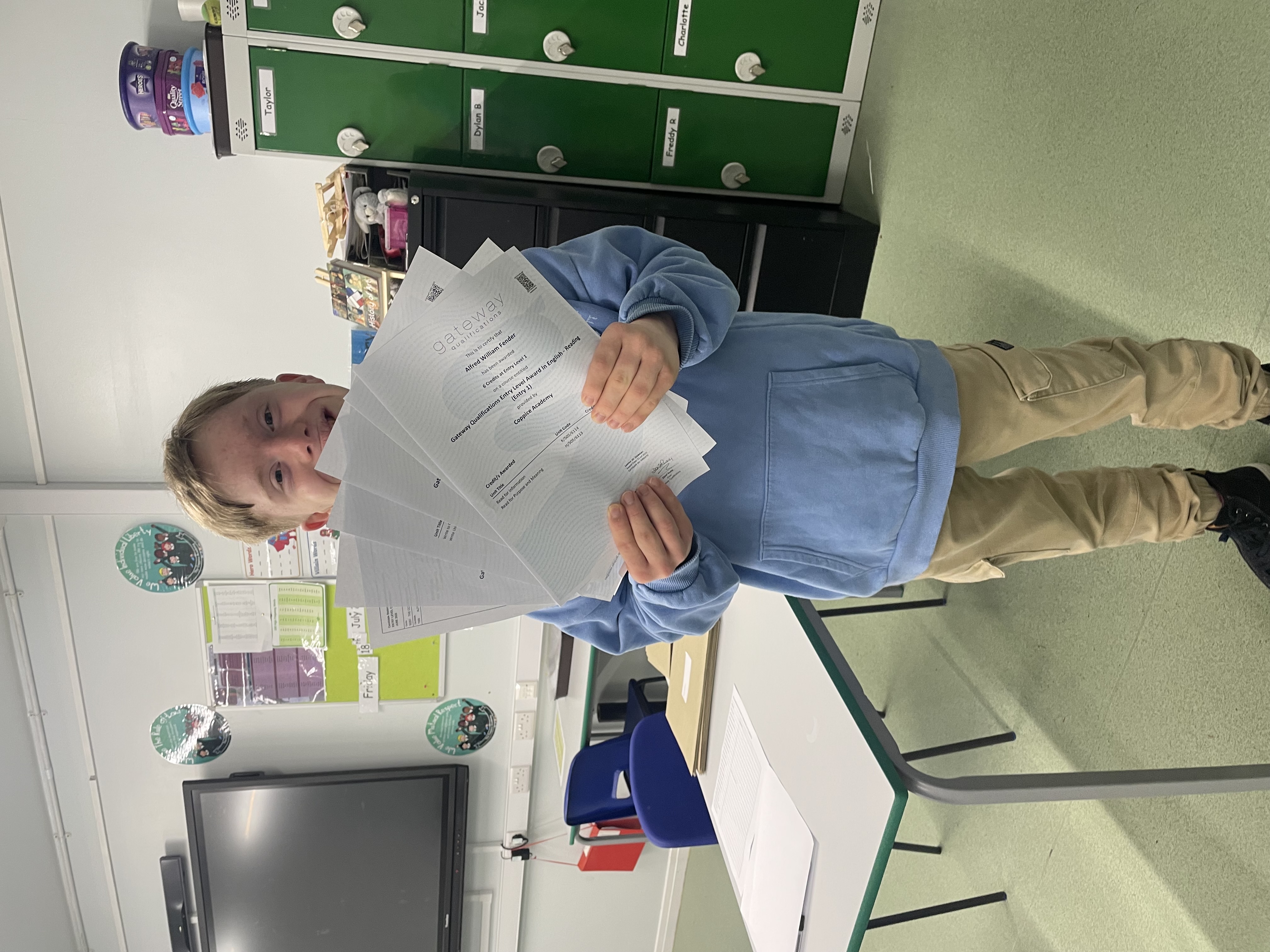 A boy in a classroom holds papers happily