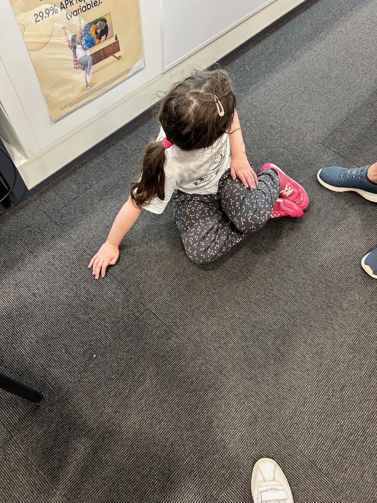 A little girl sits down on the floor of a shop aisle