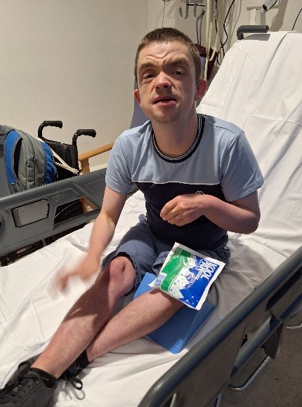 A young man sits on a hospital bed with an ice pack on his injured leg