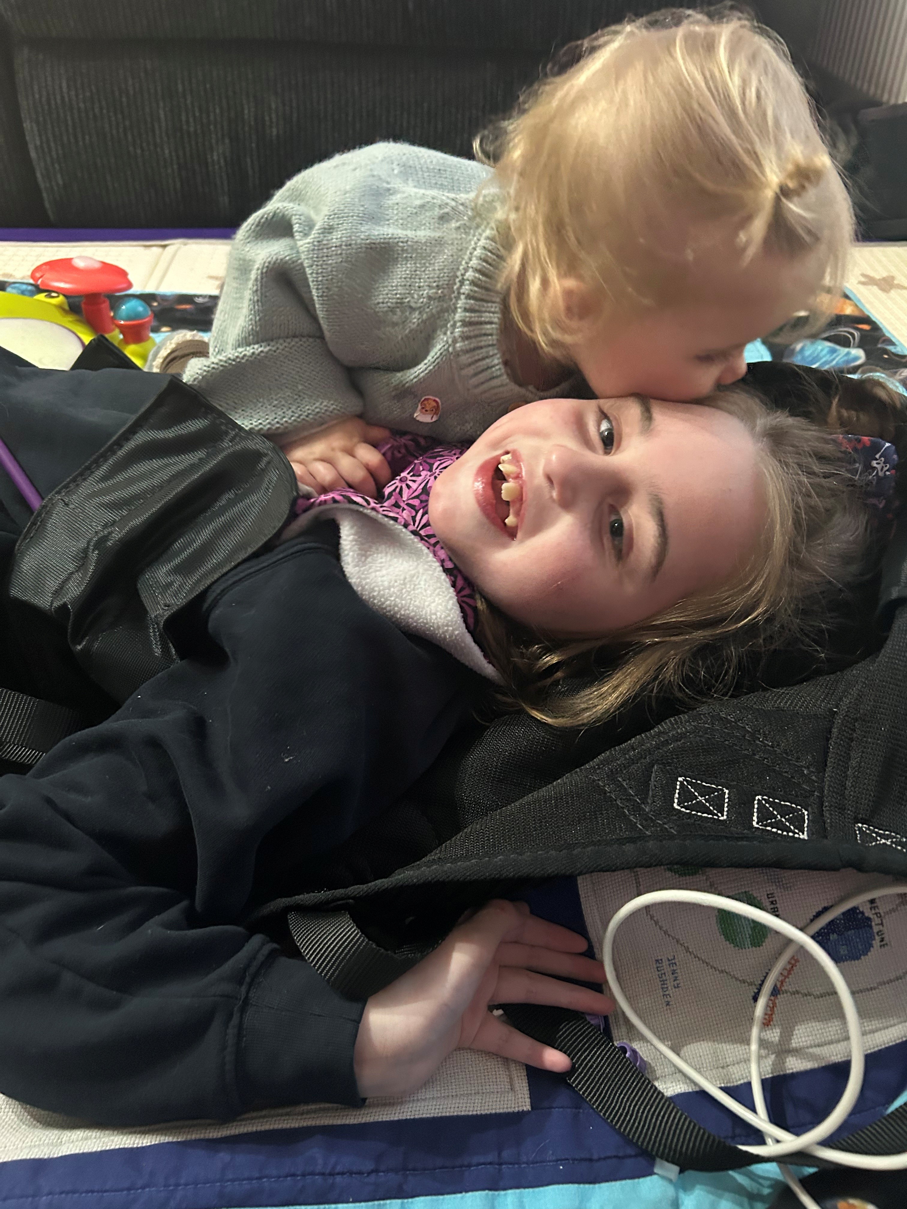 A little sister kisses her big sister on the forehead