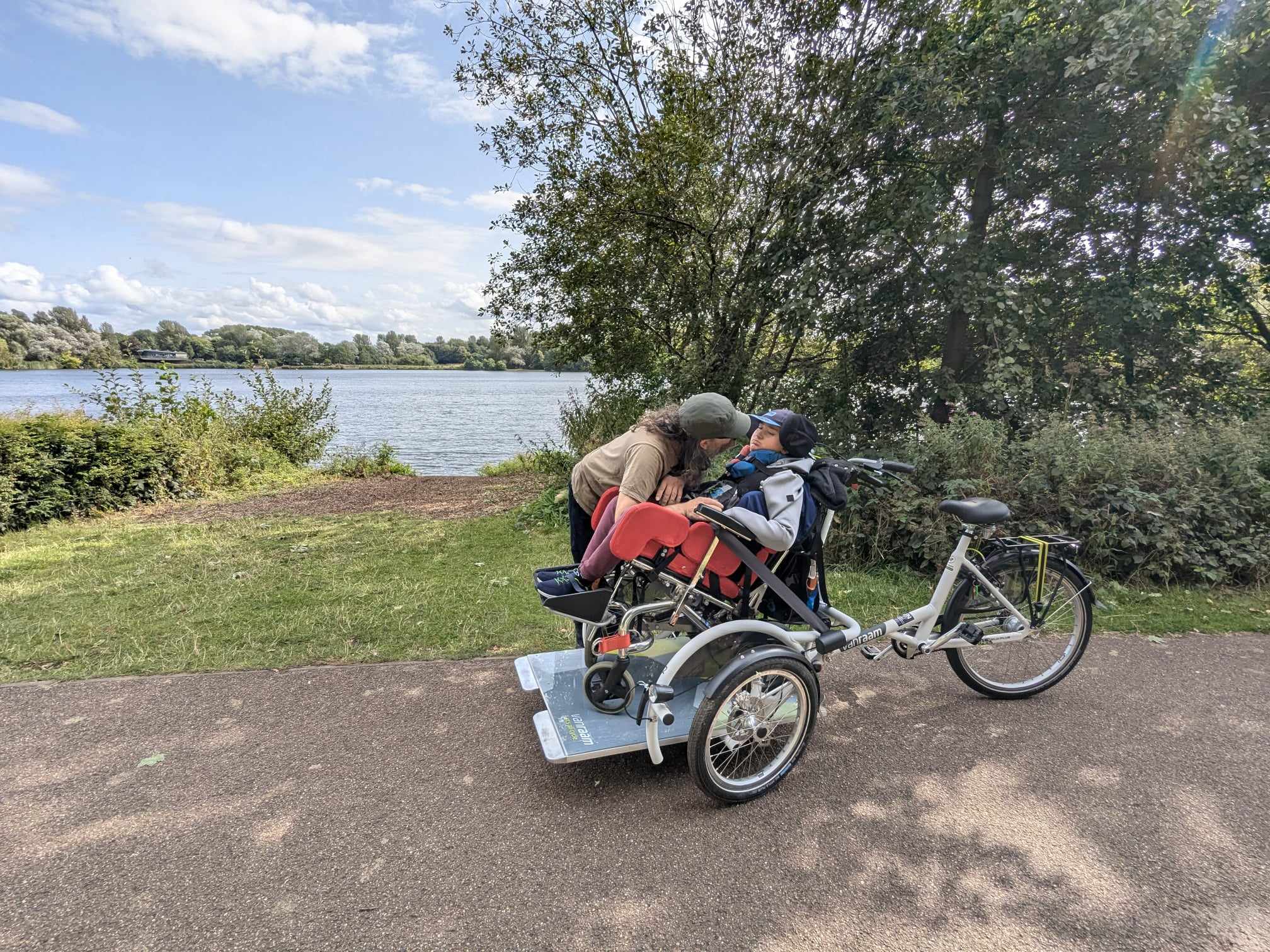 A young man sits in his wheelchair attached to a specially adapted bike (called the ‘velo’)