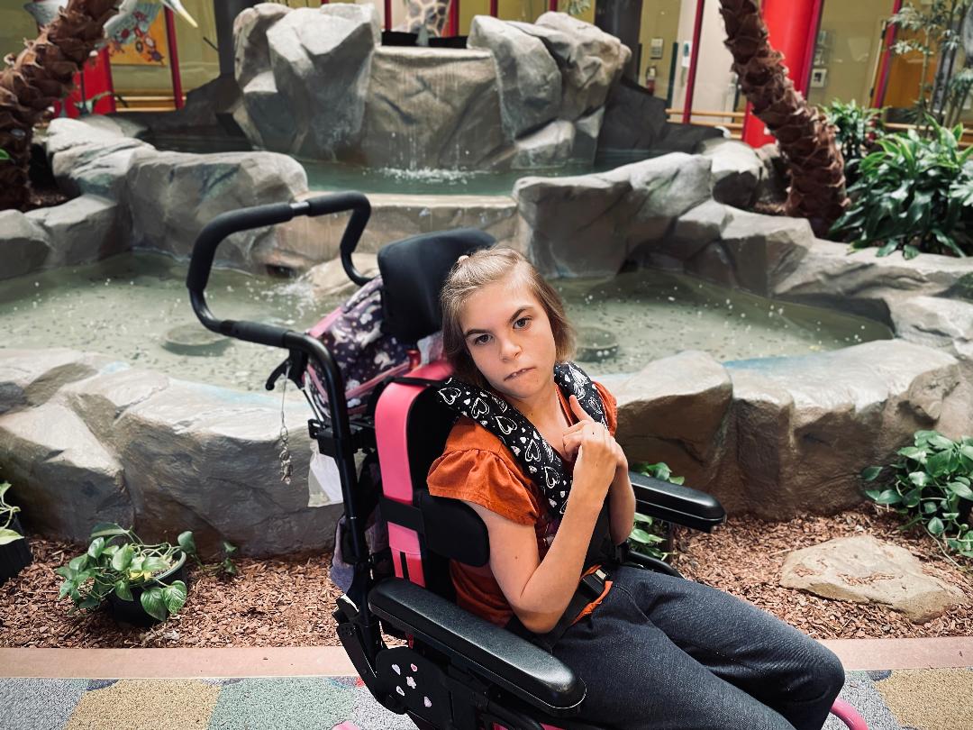 A young girl in a wheelchair by a fountain