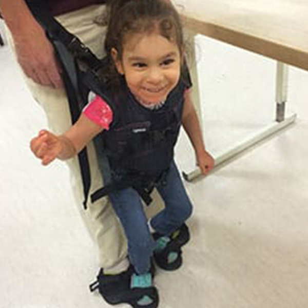 A little girl smile sin her supportive Upsee mobility harness