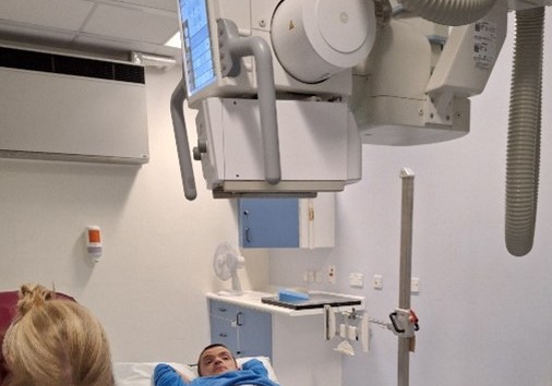 A young man is getting an X-ray on his injured leg that has a blue cast.